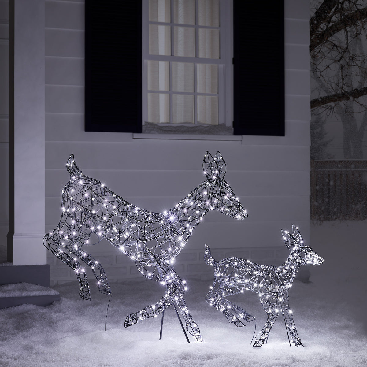 Rattan-Optik Hirschkuh und Rehkitz mit weißen LEDs vor Hausfassade im Schnee