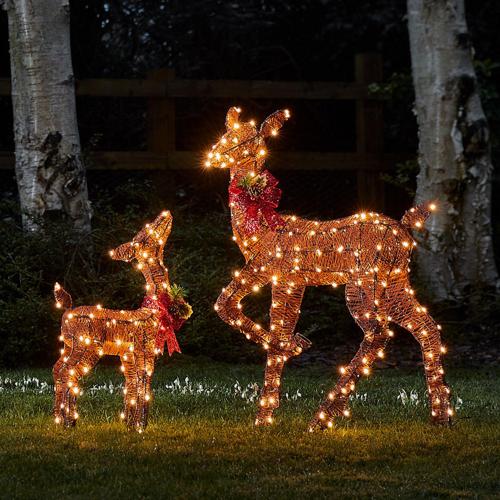 Beleuchtete braune Solar-LED-Rentiere Hirschkuh und Rehkitz mit roten Schleifen im Garten bei Nacht