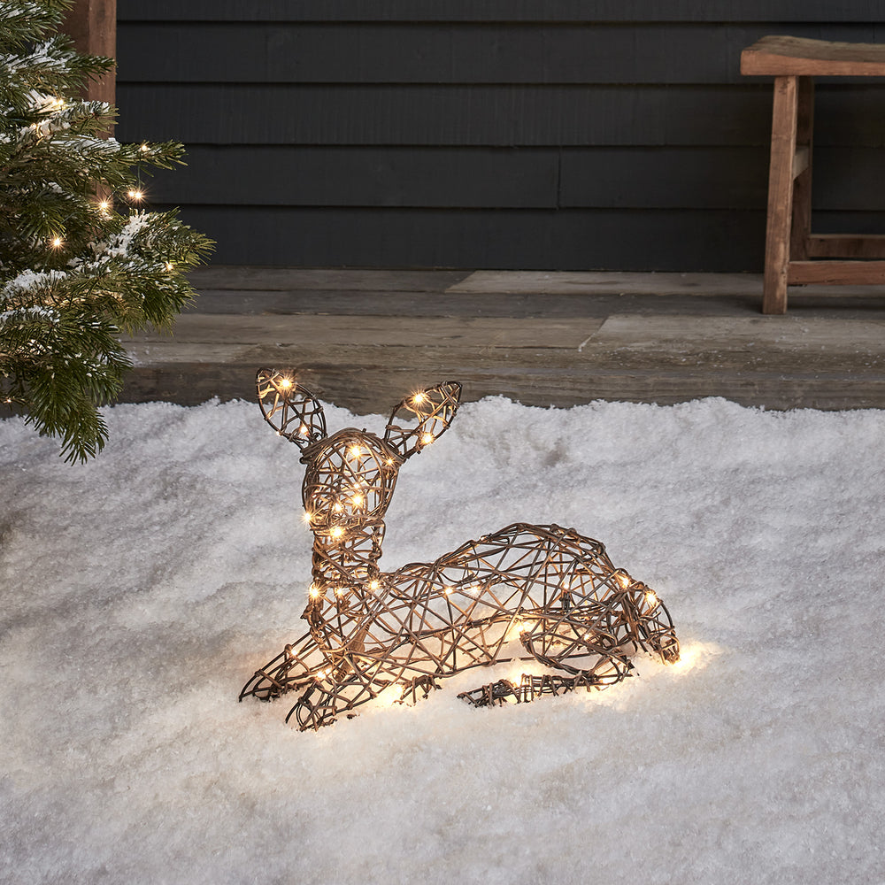 Liegendes Solar-LED-Rehkitz in brauner Rattan-Optik auf Kunstschnee vor dunkler Hauswand