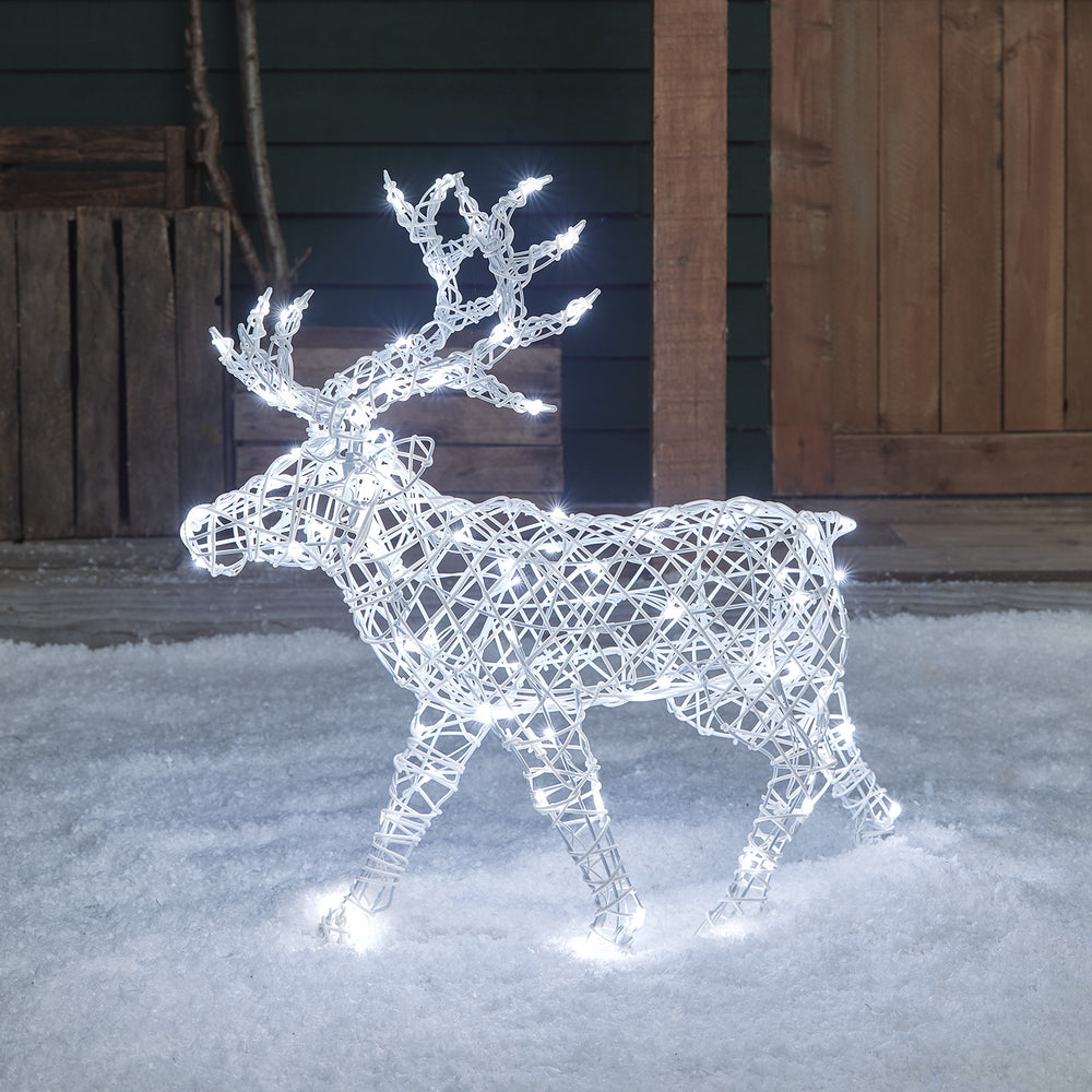 Weißes Solar-LED-Rentier in Rattan-Optik mit kaltweiß leuchtenden LEDs im Schnee vor Holzwand