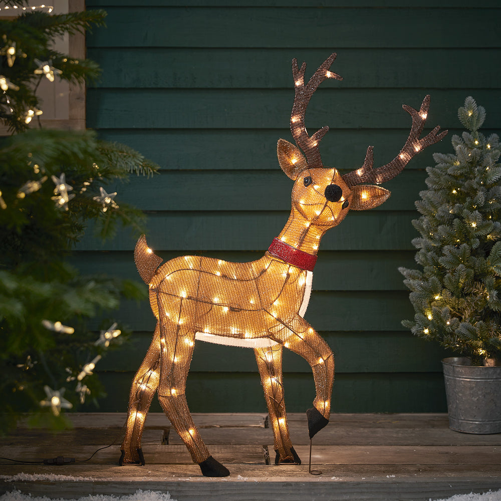 Batteriebetriebenes LED-Rentier mit rotem Schal und warmweißen Lichtern vor grünem Holzhaus