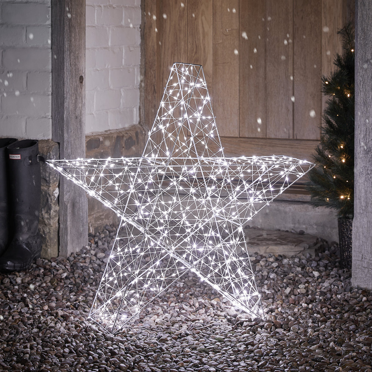 Großer 82cm hoher Bicolor LED Stern mit kaltweiß leuchtenden LEDs auf Kiesboden vor Holztür