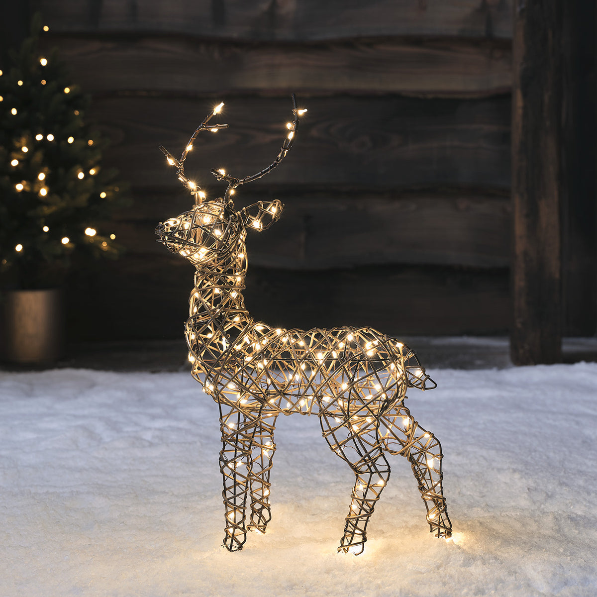 Mini Rentier aus braunem Rattanimitat mit warmweißen LEDs im Schnee vor dunklem Holzhintergrund