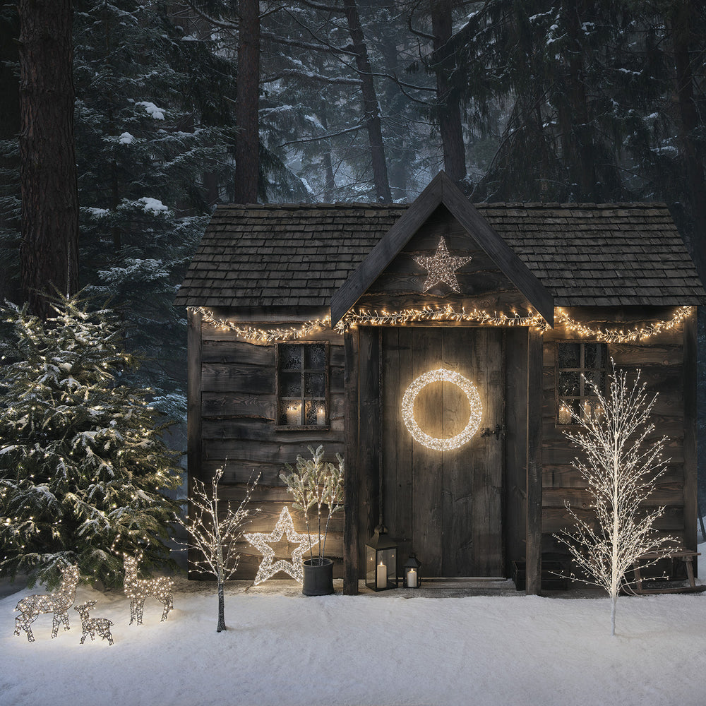 Weihnachtlich beleuchtete Holzhütte mit Sternen, Kranz und LED-Deko im verschneiten Wald
