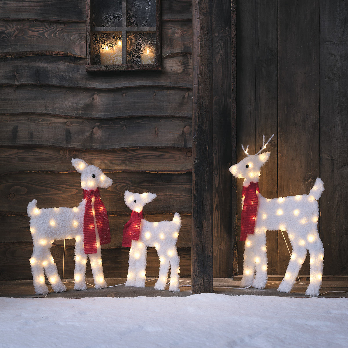 Verschneite LED-Rentierfamilie mit Vater, Mutter und Kind vor Holzwand im Schnee