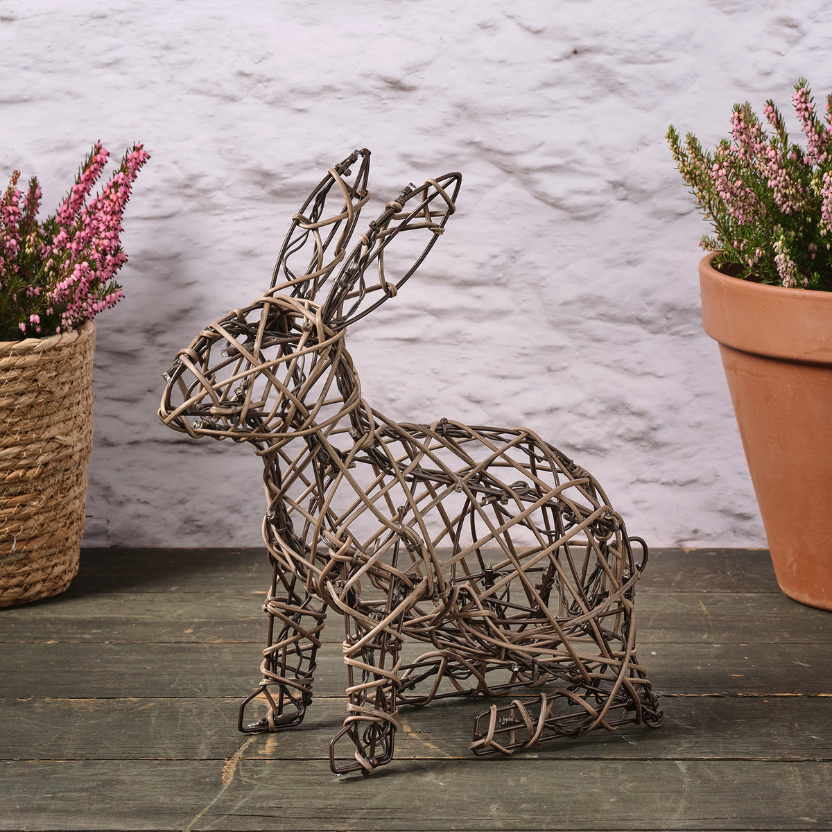 Unbeleuchteter Rattan-Hase auf dunklem Holzboden mit Blumentopf im Hintergrund
