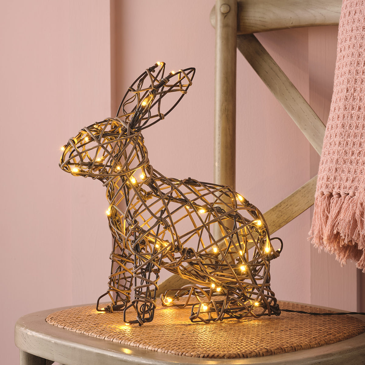 Beleuchteter Rattan-Hase auf Stuhl mit rosa Wand und rosa Decke im Hintergrund