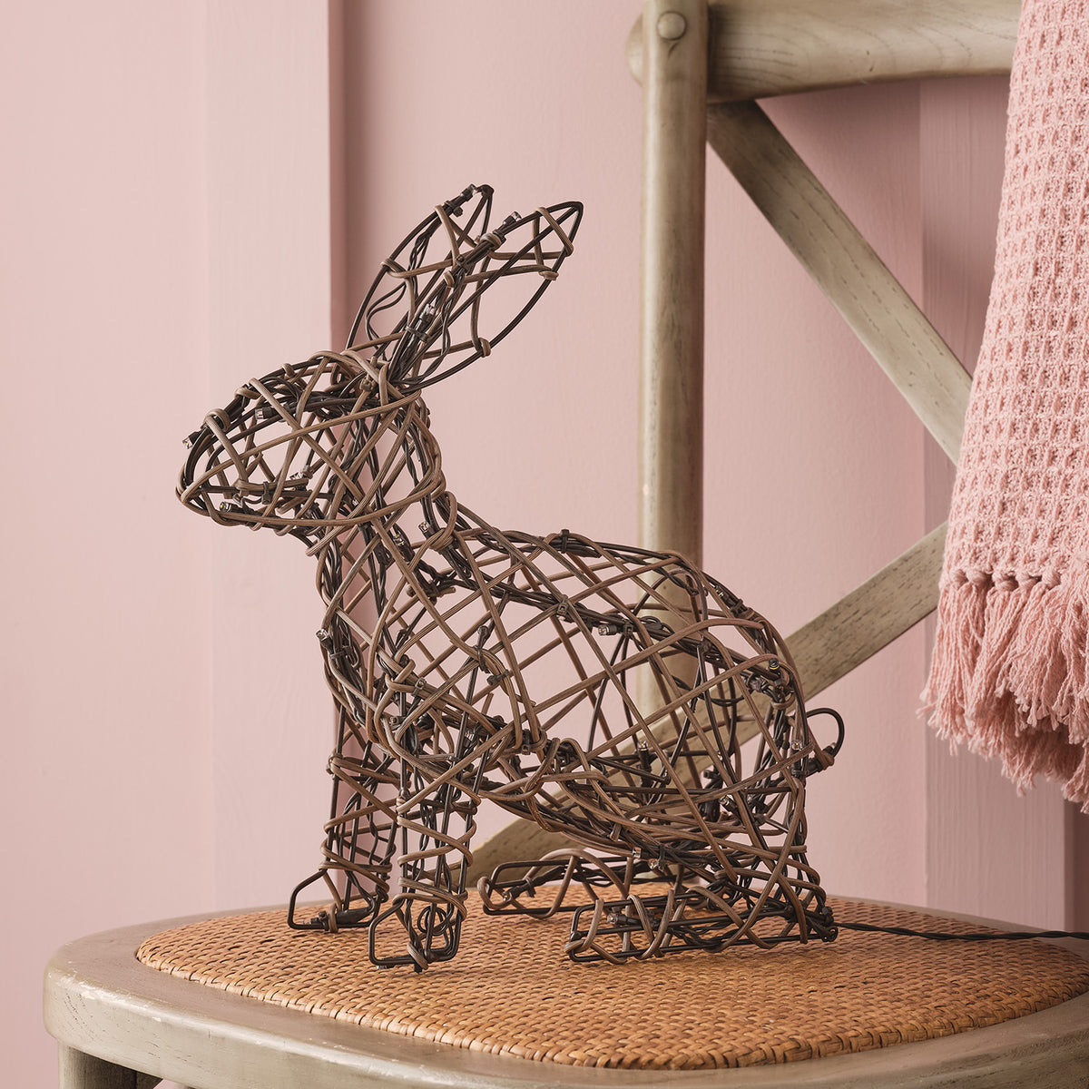Unbeleuchteter Rattan-Hase auf Stuhl vor rosa Wand mit rosa Decke