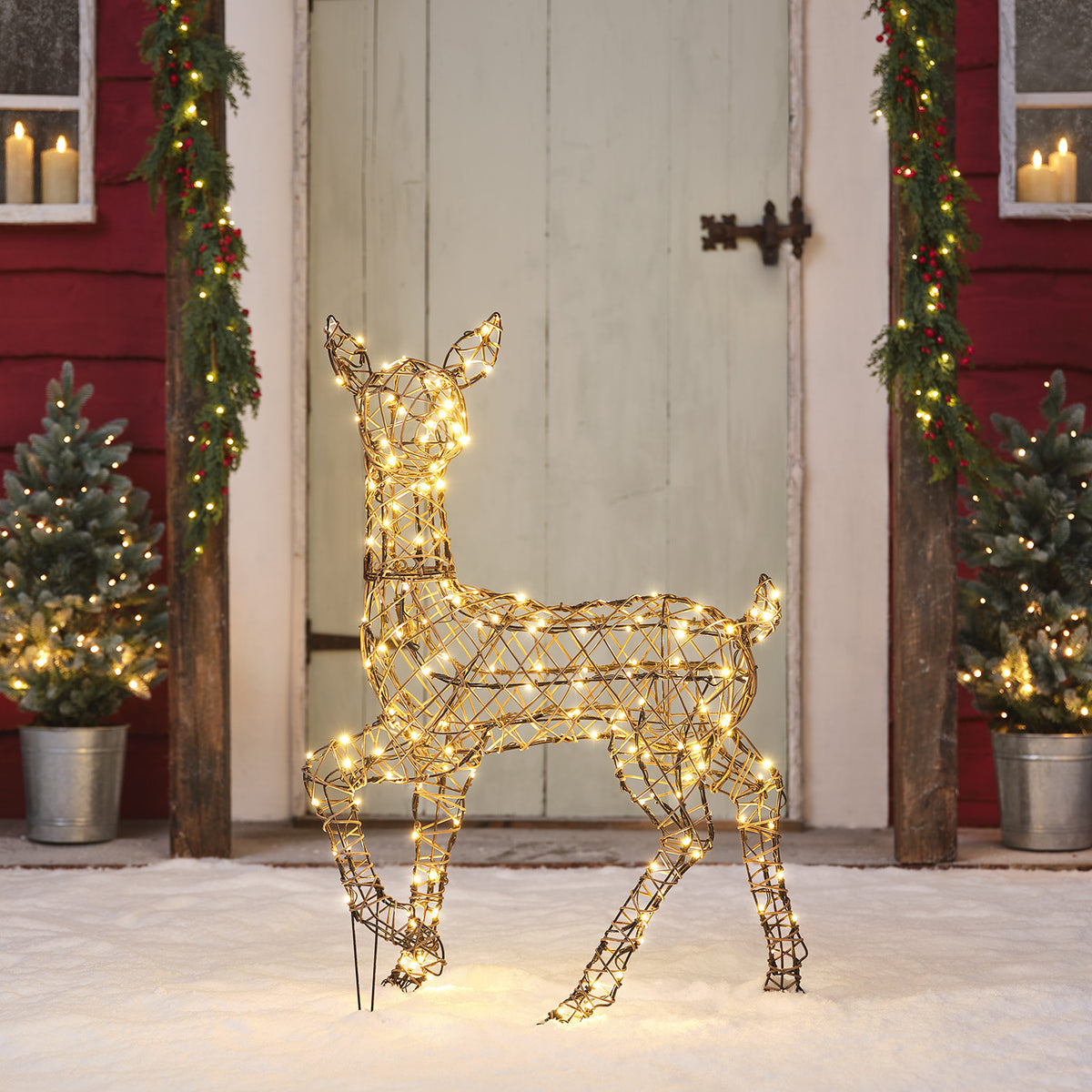 LED-Rentier aus geflochtenem Kunst-Rattan mit warmweißen Lichtern vor Haustür im Schnee