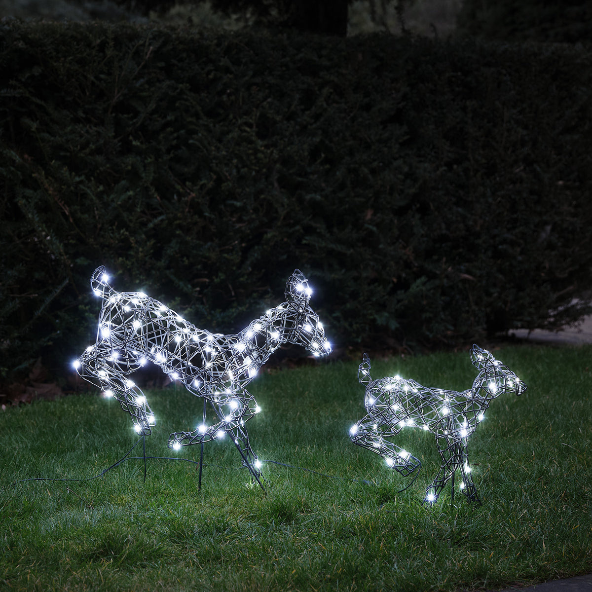 LED-Rentiere Hirschkuh und Rehkitz mit kaltweißen Lichtern auf grünem Rasen bei Dunkelheit, Nahaufnahme
