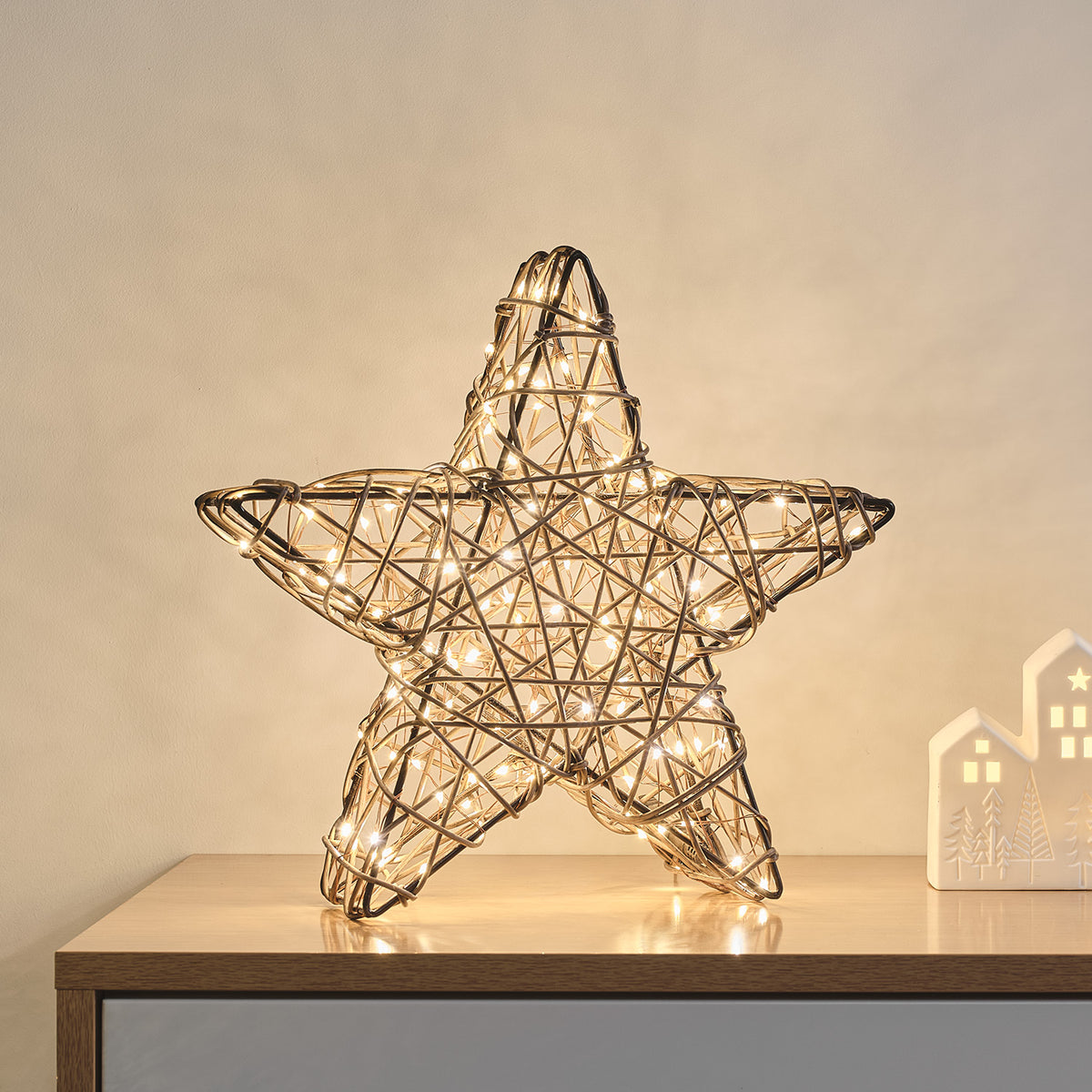 Nahaufnahme des beleuchteten Rattan-LED-Sterns auf einem Sideboard mit Dekoration