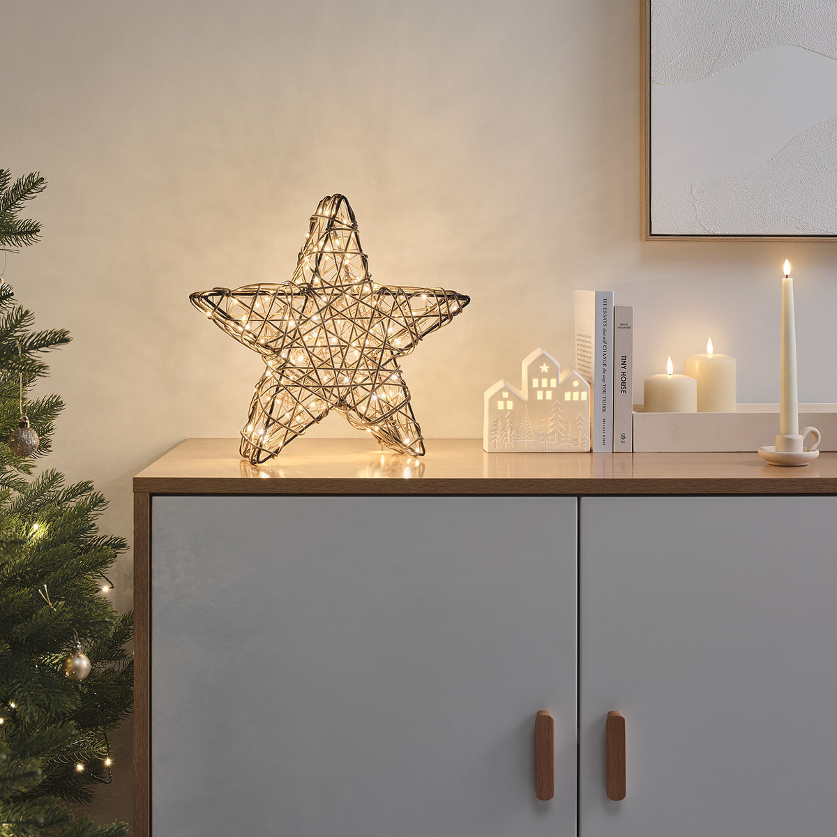 Rattan-LED-Stern auf Sideboard neben Kerzen und Weihnachtsdeko in warmem Licht