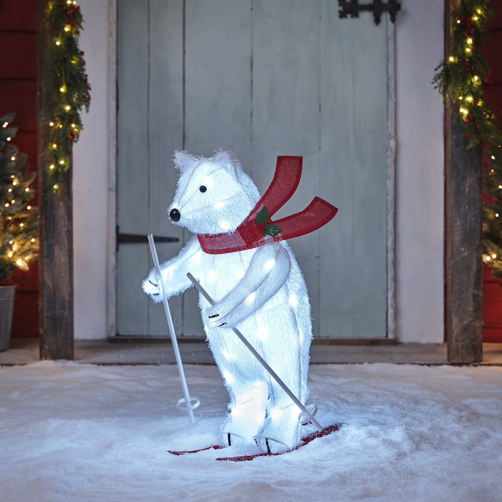 Bewegliche LED-Polarbär-Figur mit roten Skiern und Skistöcken im Schnee vor Holztür