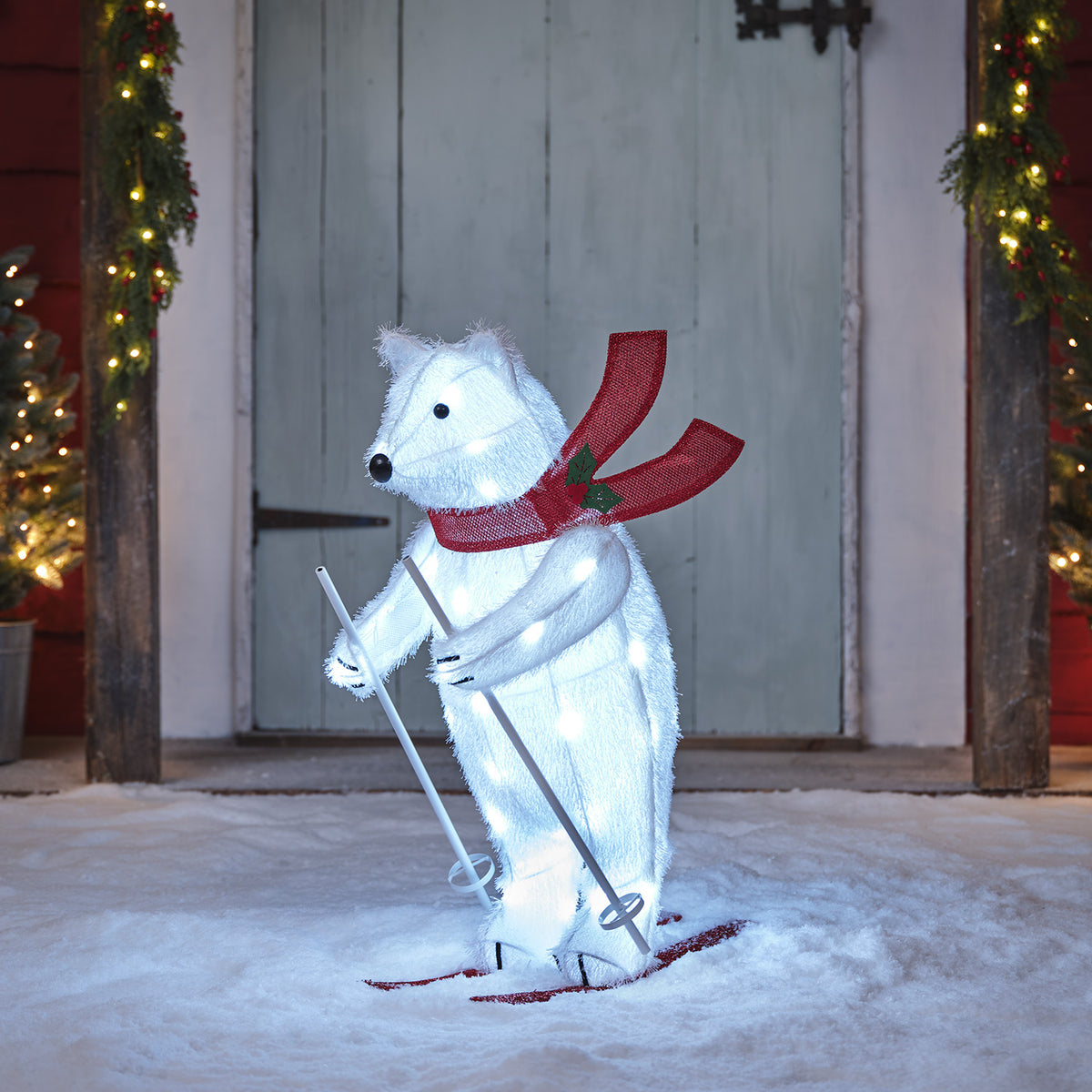 Weihnachtsfigur Polarbär mit LED-Beleuchtung, rotem Schal und Skiern auf Schnee stehend