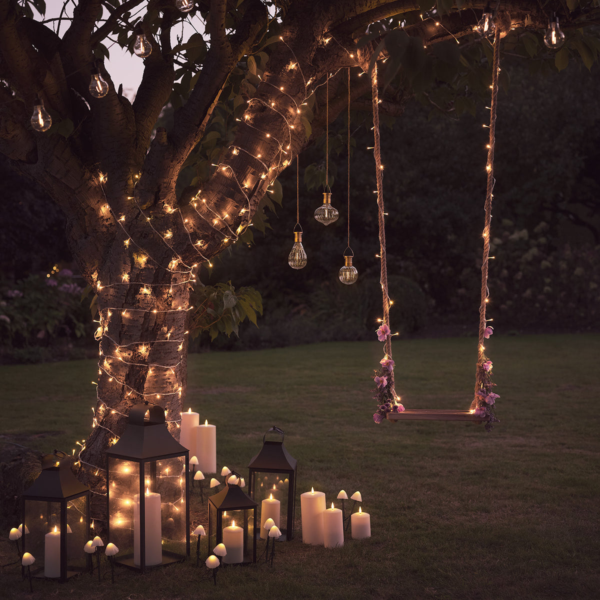 Gartenbaum mit Lichterketten, Laternen und Solar-Pilzleuchten am Boden