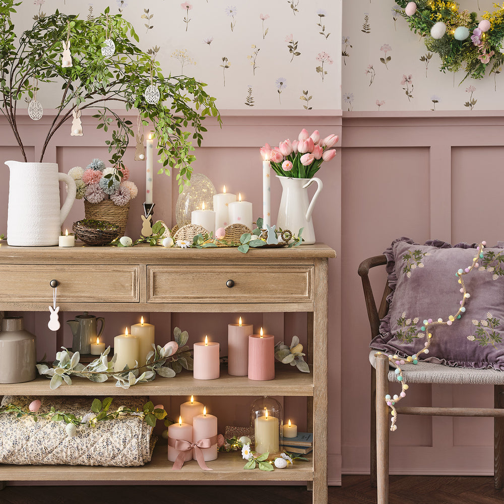 Ostertisch mit Glasosterei, Kerzen, Blumen und Frühlingsdeko vor rosa Wand