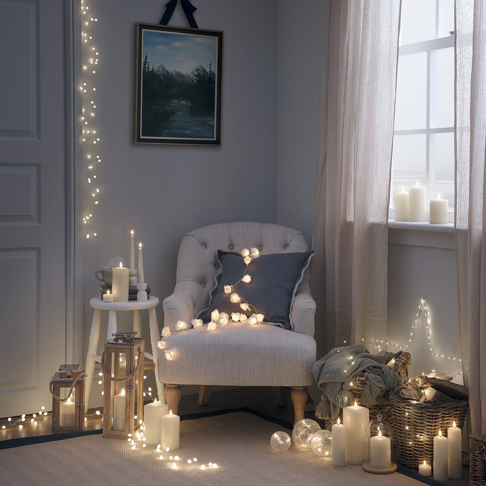 Gemütliches Wohnzimmer mit Lichterkette, Kerzen und Sessel mit Kissen und Decke