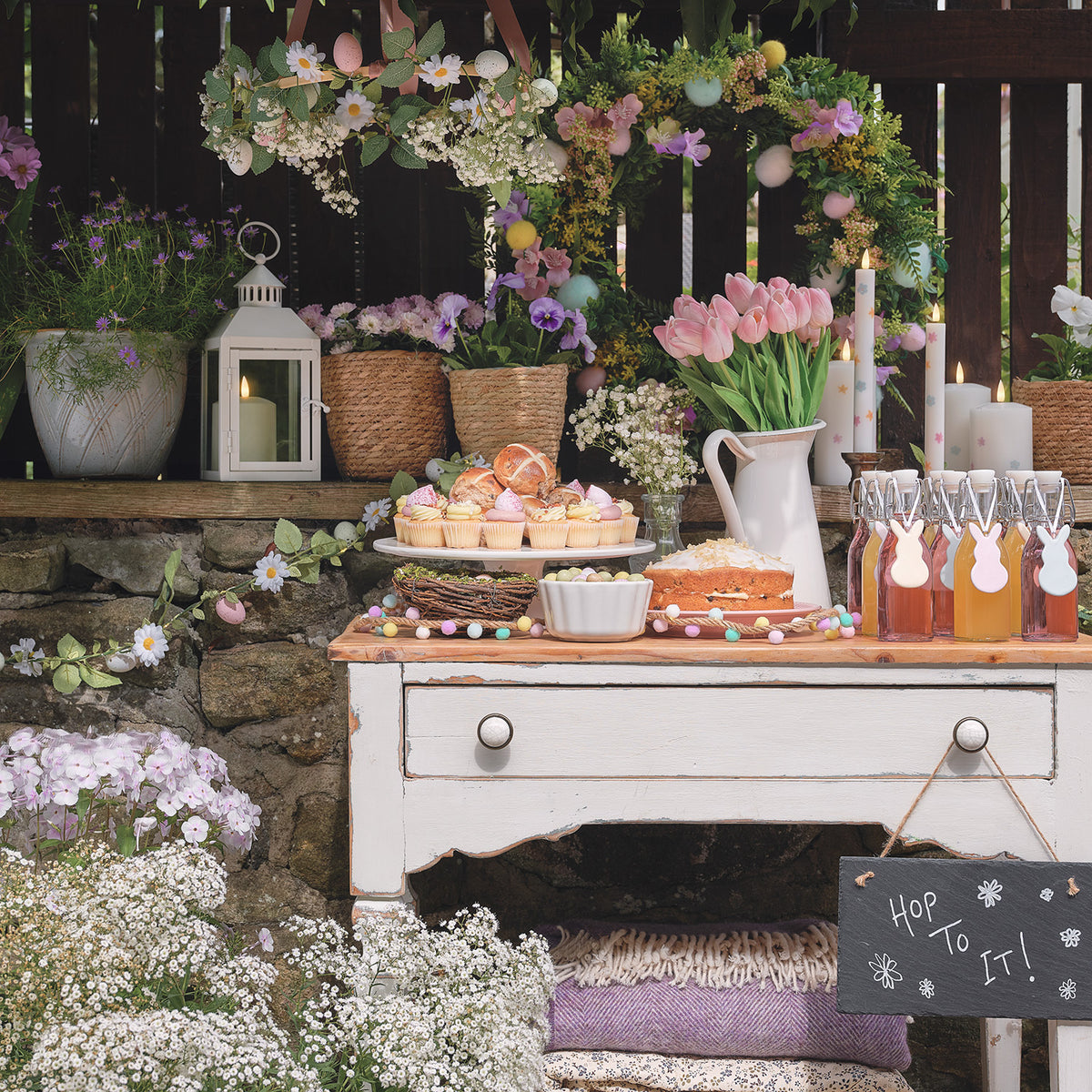 Frühlingsdeko mit Keramik-Hasen an Flaschen, Kuchen und Blumen auf Holztisch