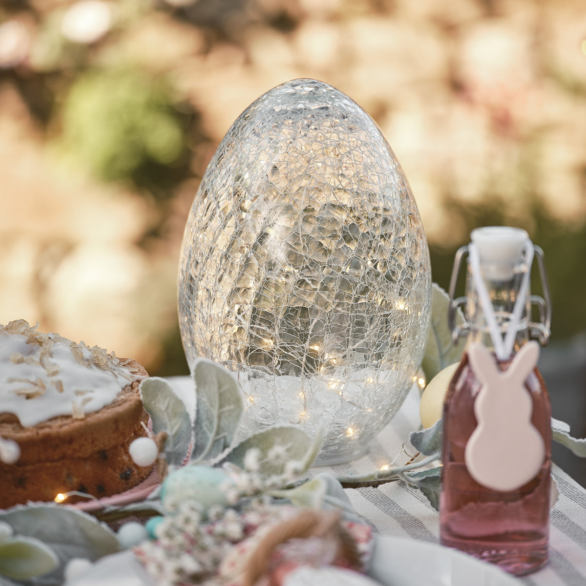 Großes Glas-Ei mit Lichterkette und Keramik-Hase auf gedecktem Ostertisch