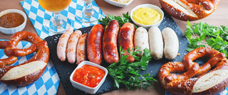 Two glasses of beer, pretzels, sausages, and bread on a wooden table.