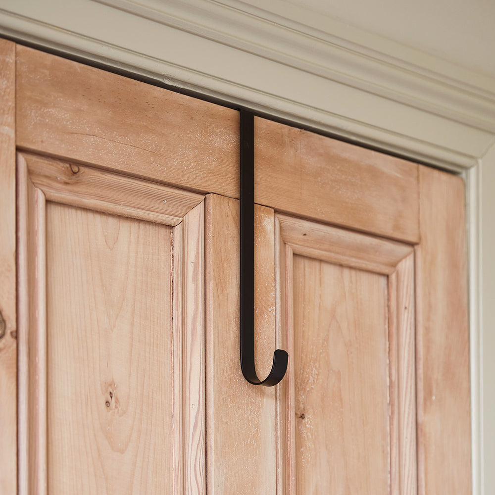 Schwarzer Türhaken aus Metall hängt über einer hellen Holztür