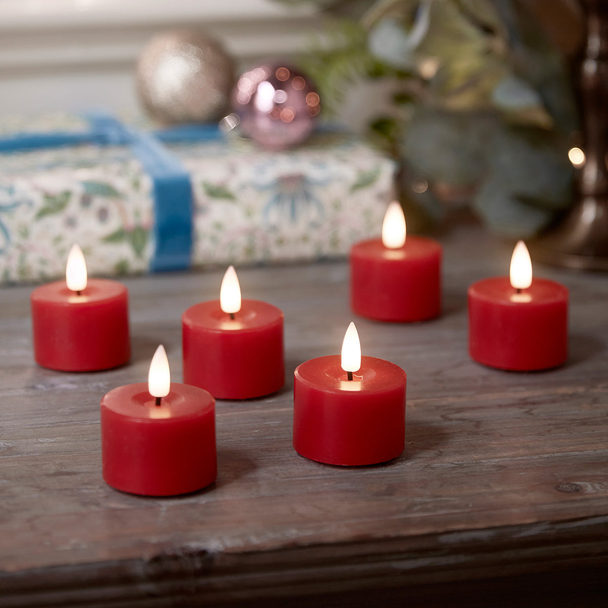Sechs rote LED Votivkerzen aus Echtwachs mit flackernder Flamme auf Holztisch vor Weihnachtsdeko