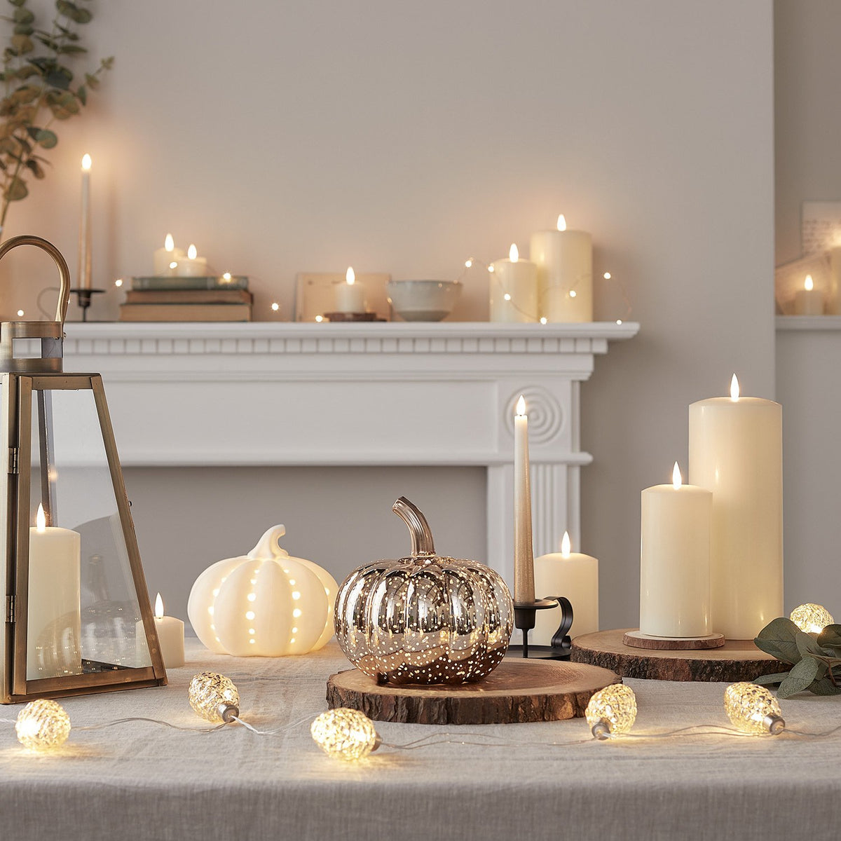 Weißer Keramik Kürbis mit LED-Licht auf Holztisch mit Kerzen und Herbstdeko