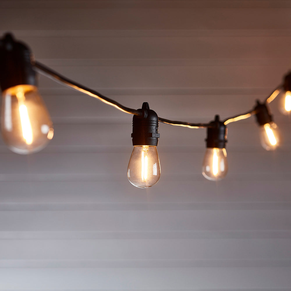 Nahaufnahme einer warmweißen LED-Glühbirne an schwarzem Kabel vor grauer Wand