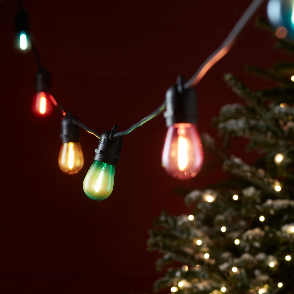 Nahaufnahme bunter LED-Glühbirnen an schwarzem Kabel vor roter Wand