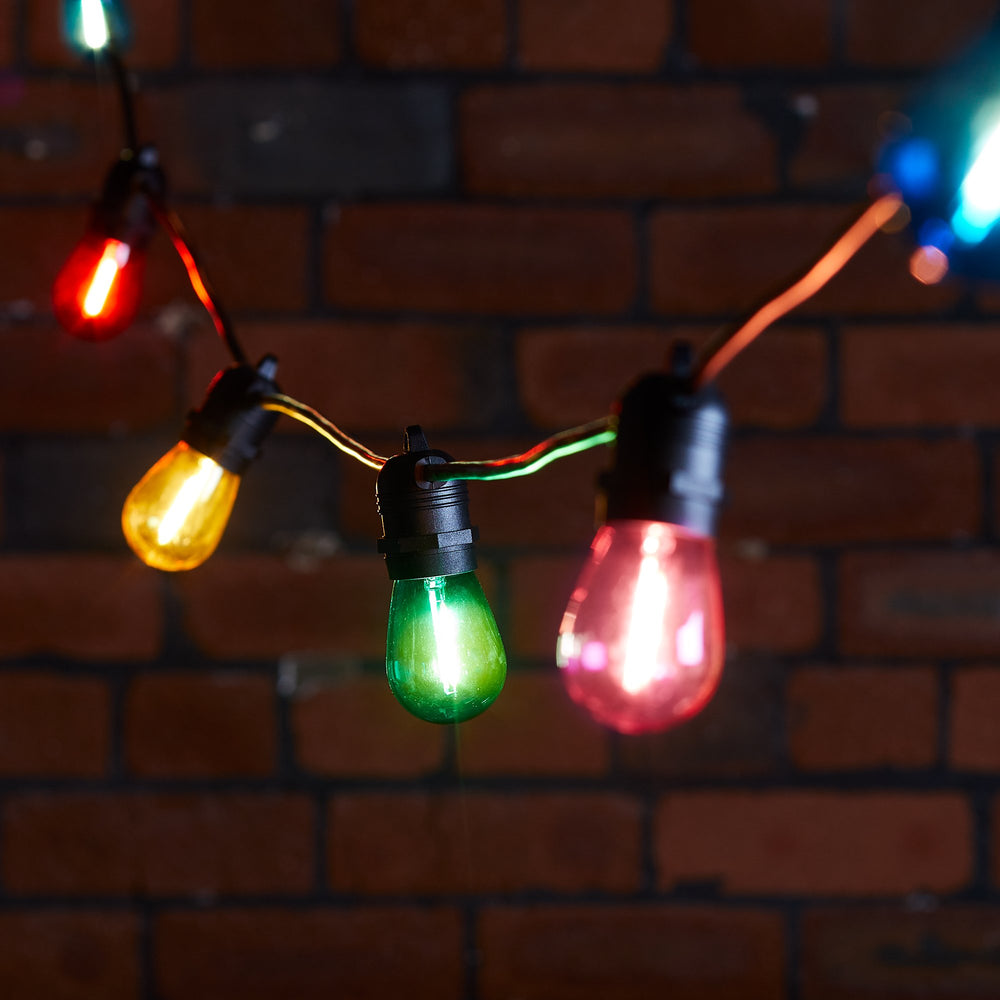 Bunte LED-Glühbirnen an schwarzem Kabel vor roter Backsteinwand