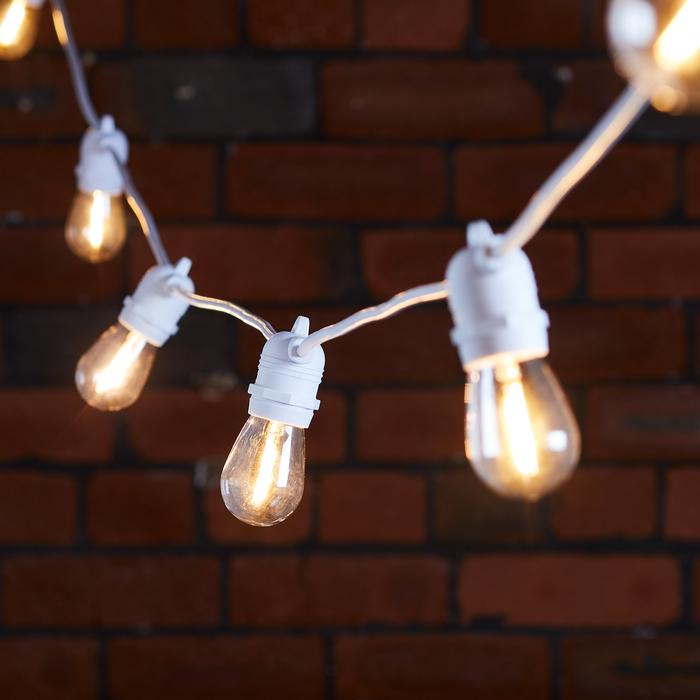 Warmweiße Glühbirnen an weißem Kabel vor roter Backsteinwand