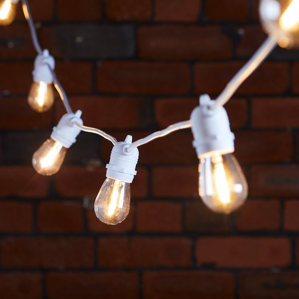 Warmweiße LED-Glühbirnen an weißem Kabel vor roter Backsteinwand in Innenraum
