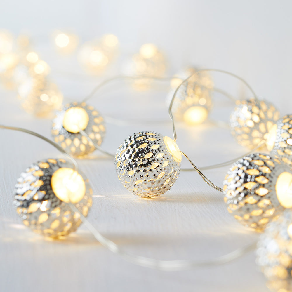 Leuchtende Micro Lichterkette mit marokkanischen Metallkugeln und warmweißem Licht auf hellem Untergrund