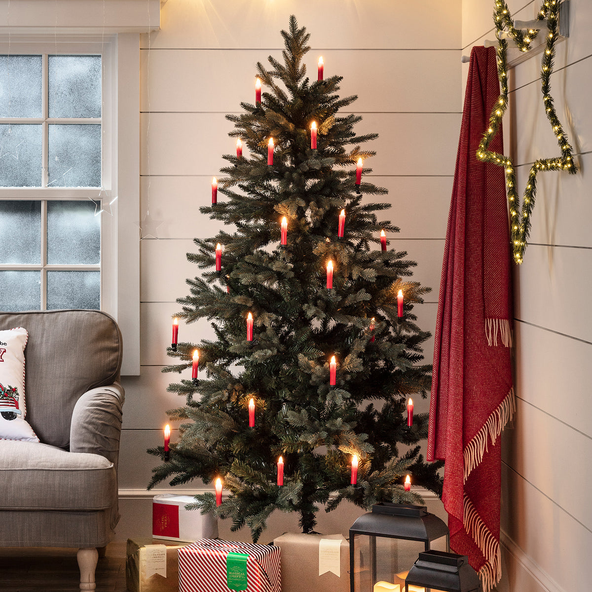 Weihnachtsbaum mit roten LED-Kerzen in einem gemütlichen Wohnzimmer mit Geschenken und Dekoration