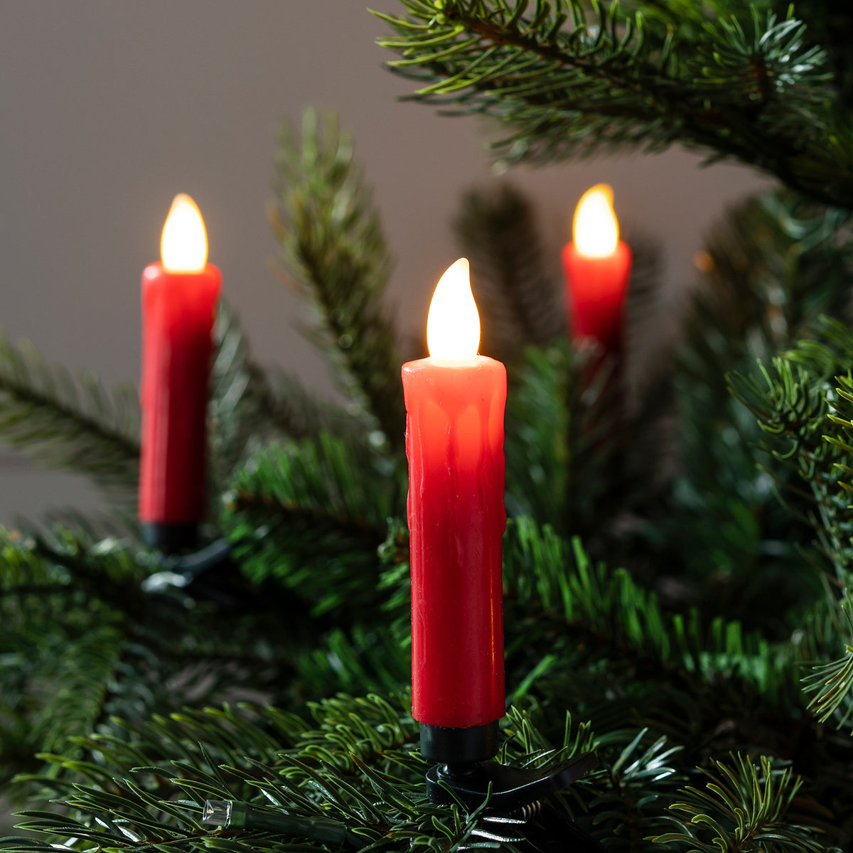 Nahaufnahme von drei roten LED-Weihnachtsbaumkerzen mit flackernder Flamme an Tannenzweigen