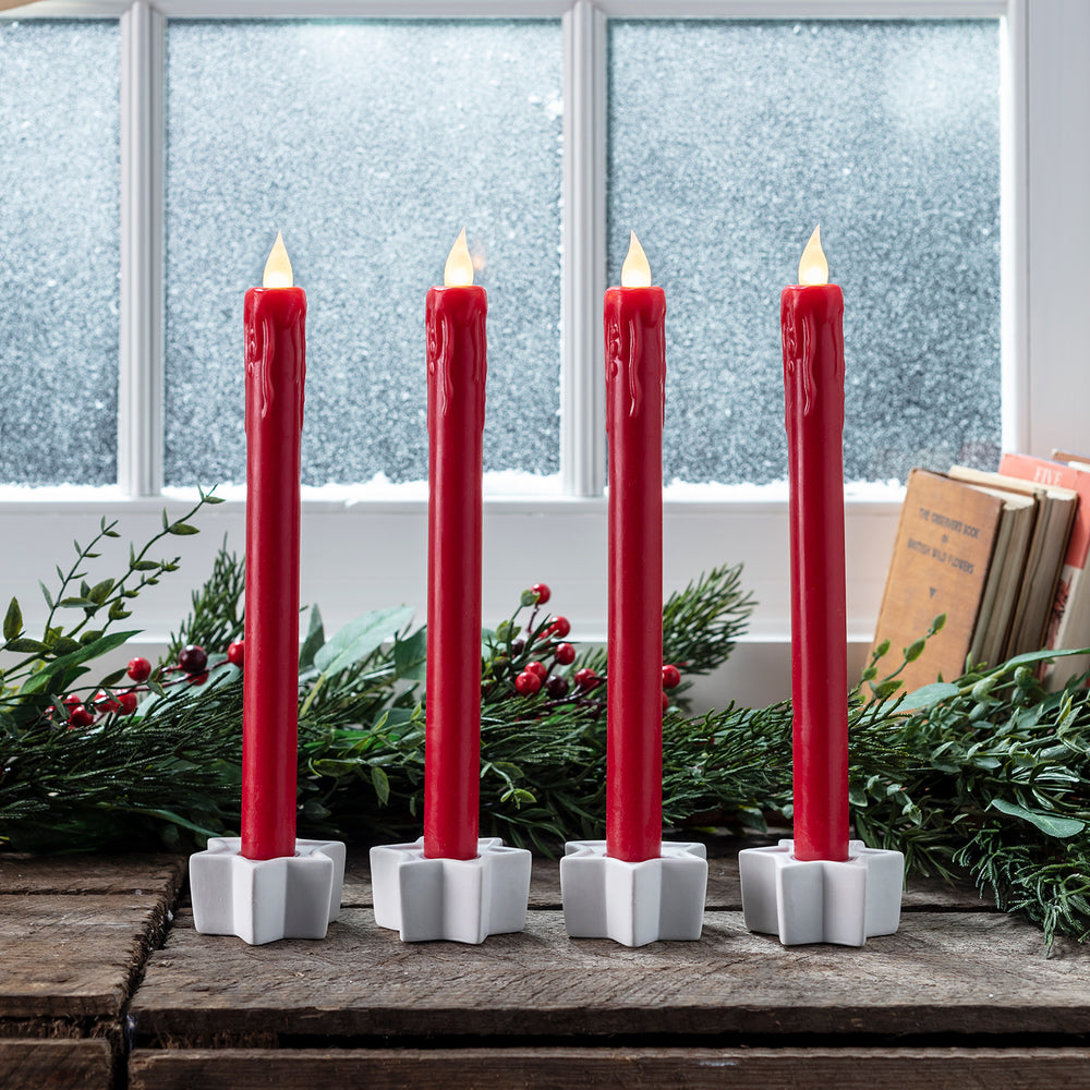 Vier rote LED Stabkerzen mit flackernder Flamme in weißen sternförmigen Kerzenhaltern vor Fenster mit Schnee