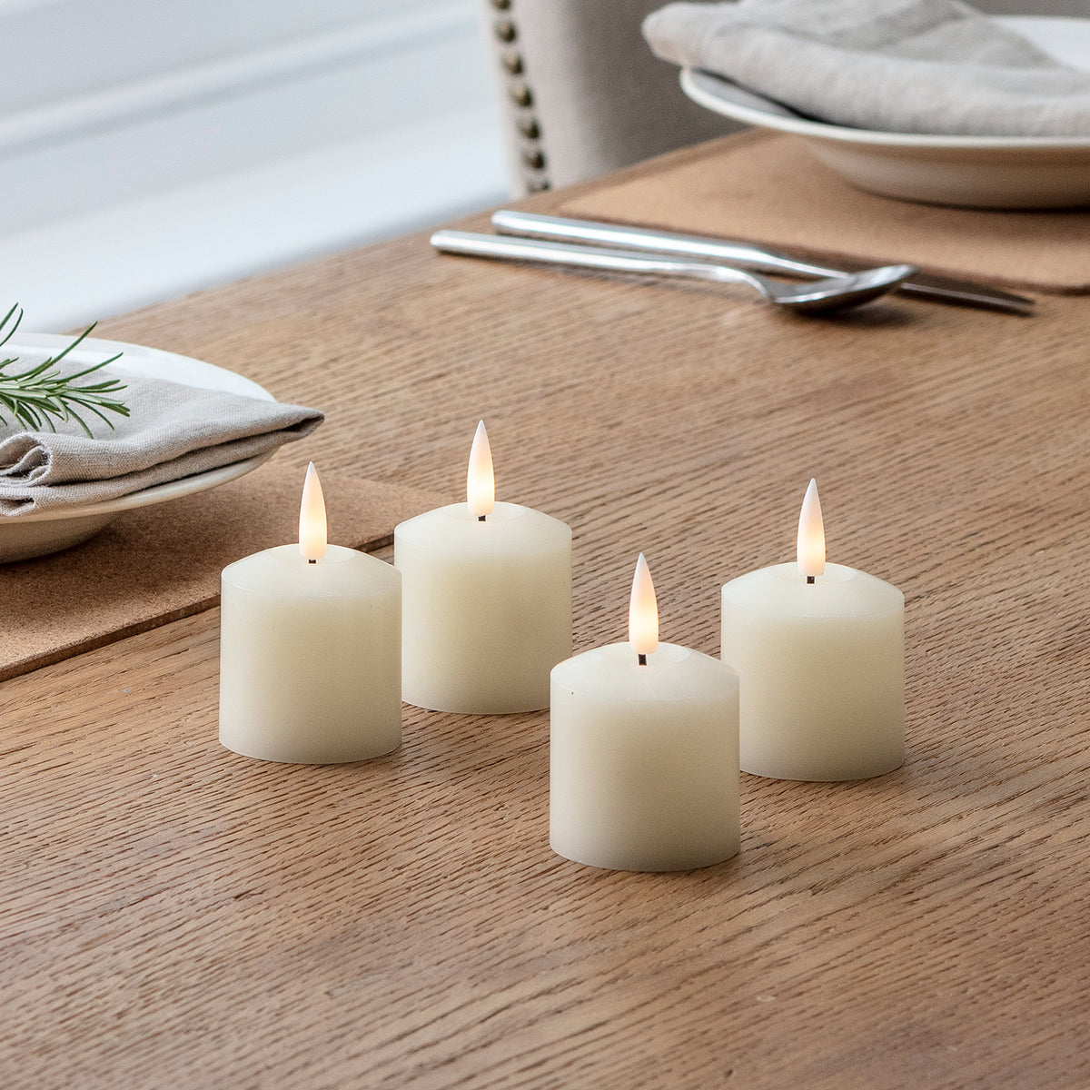 Vier LED Votivkerzen auf einem Holztisch mit Besteck und grauem Stoffserviette im Hintergrund