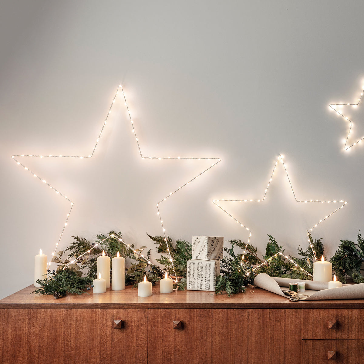 LED Stumpenkerzen vor Wand mit beleuchteten Sternen aus Lichterketten