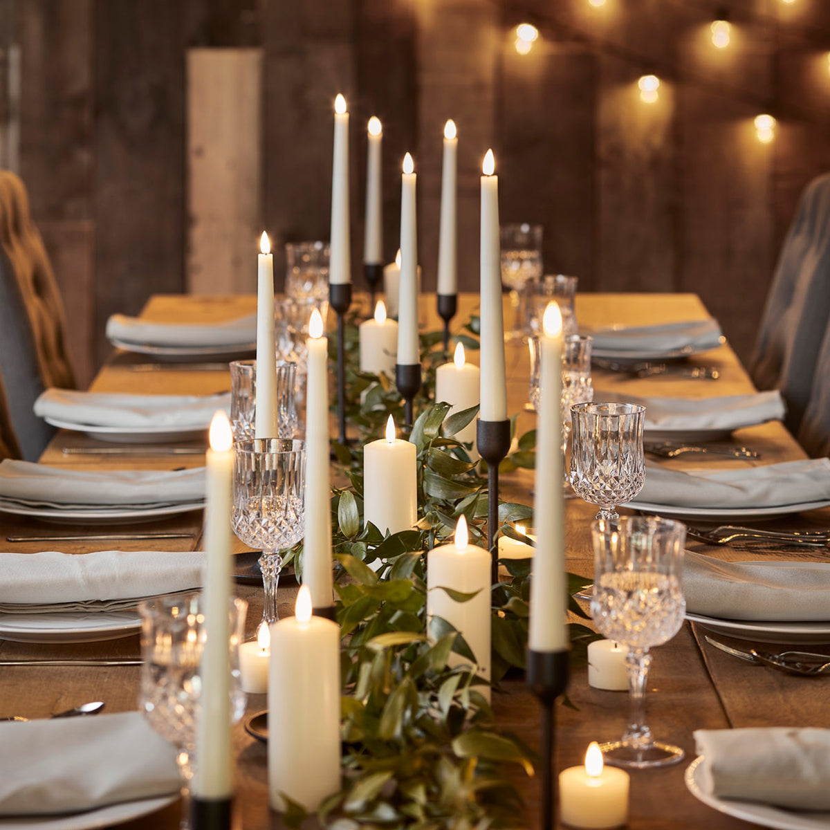 Elfenbeinfarbene LED Hochzeitskerzen auf einem festlich gedeckten Holztisch mit grüner Dekoration