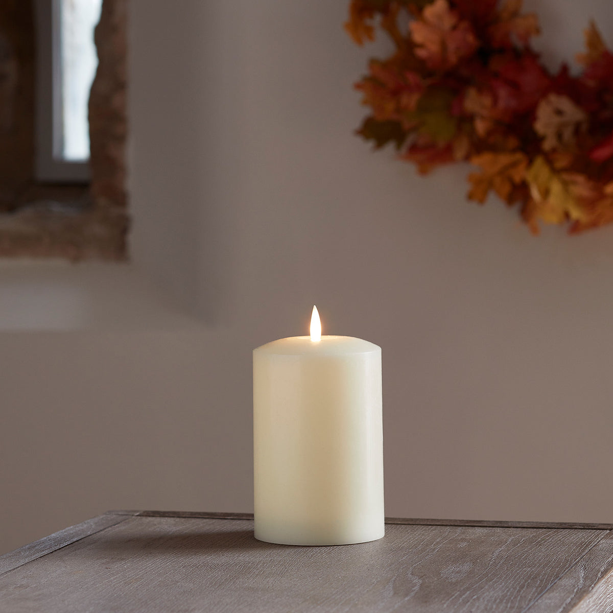 LED Stumpenkerze mit flackernder Flamme auf Holztisch vor herbstlicher Wanddekoration