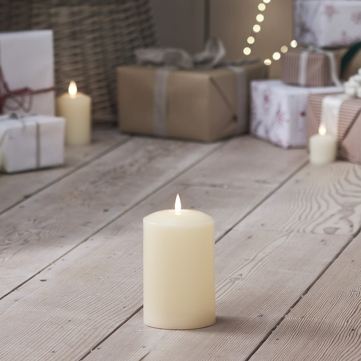 LED Stumpenkerze auf hellem Holzboden vor Weihnachtsgeschenken und Dekoration
