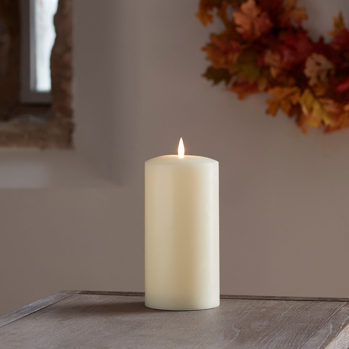 TruGlow LED Stumpenkerze mit flackernder Flamme vor herbstlicher Wanddekoration