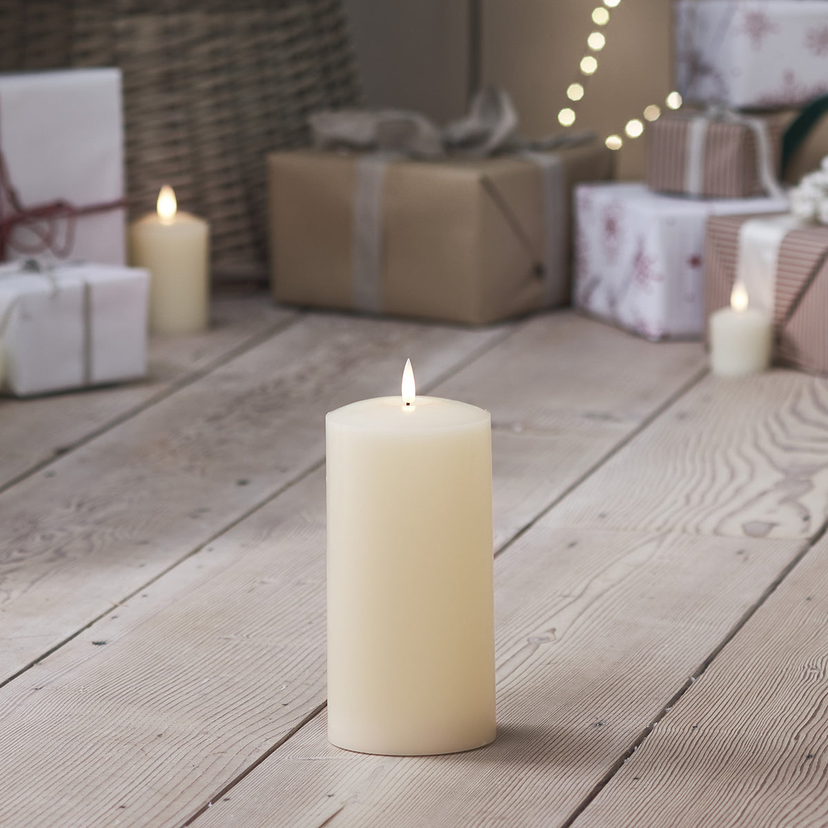TruGlow LED Stumpenkerze mit flackernder Flamme vor weihnachtlich verpackten Geschenken