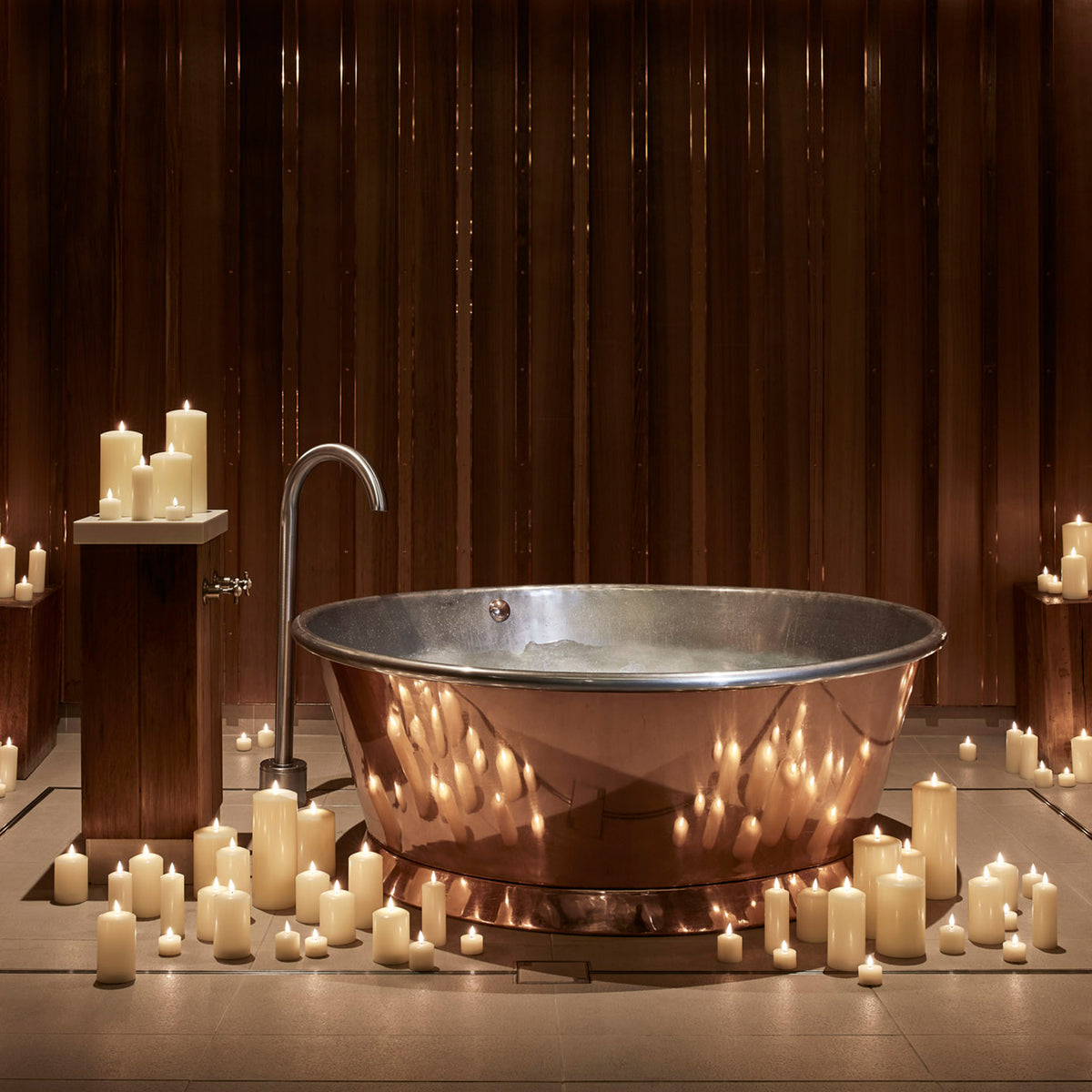 Kupferbadewanne umgeben von zahlreichen TruGlow LED Stumpenkerzen in einem Spa-Raum