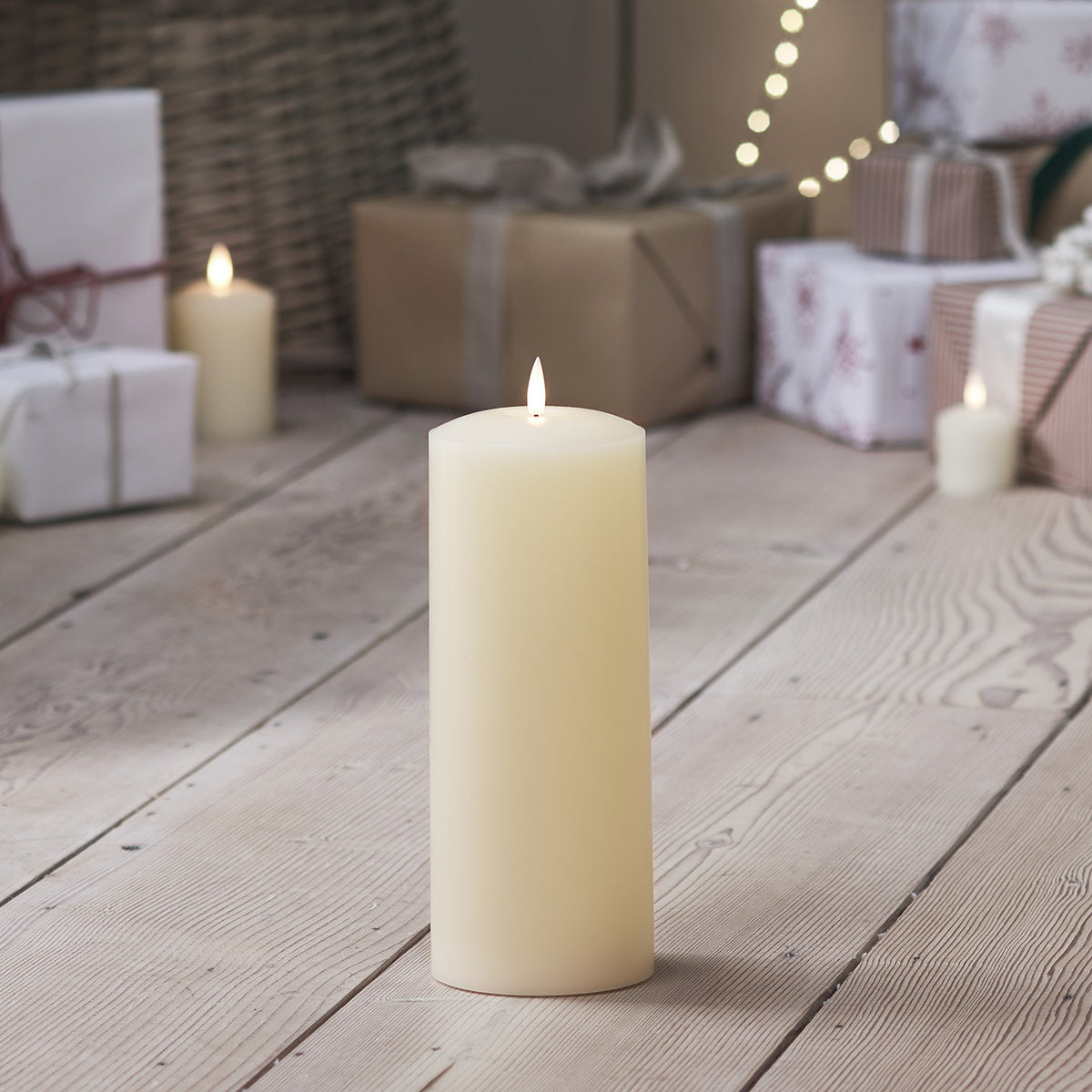 TruGlow LED Stumpenkerze auf hellem Holzboden mit Weihnachtsgeschenken im Hintergrund