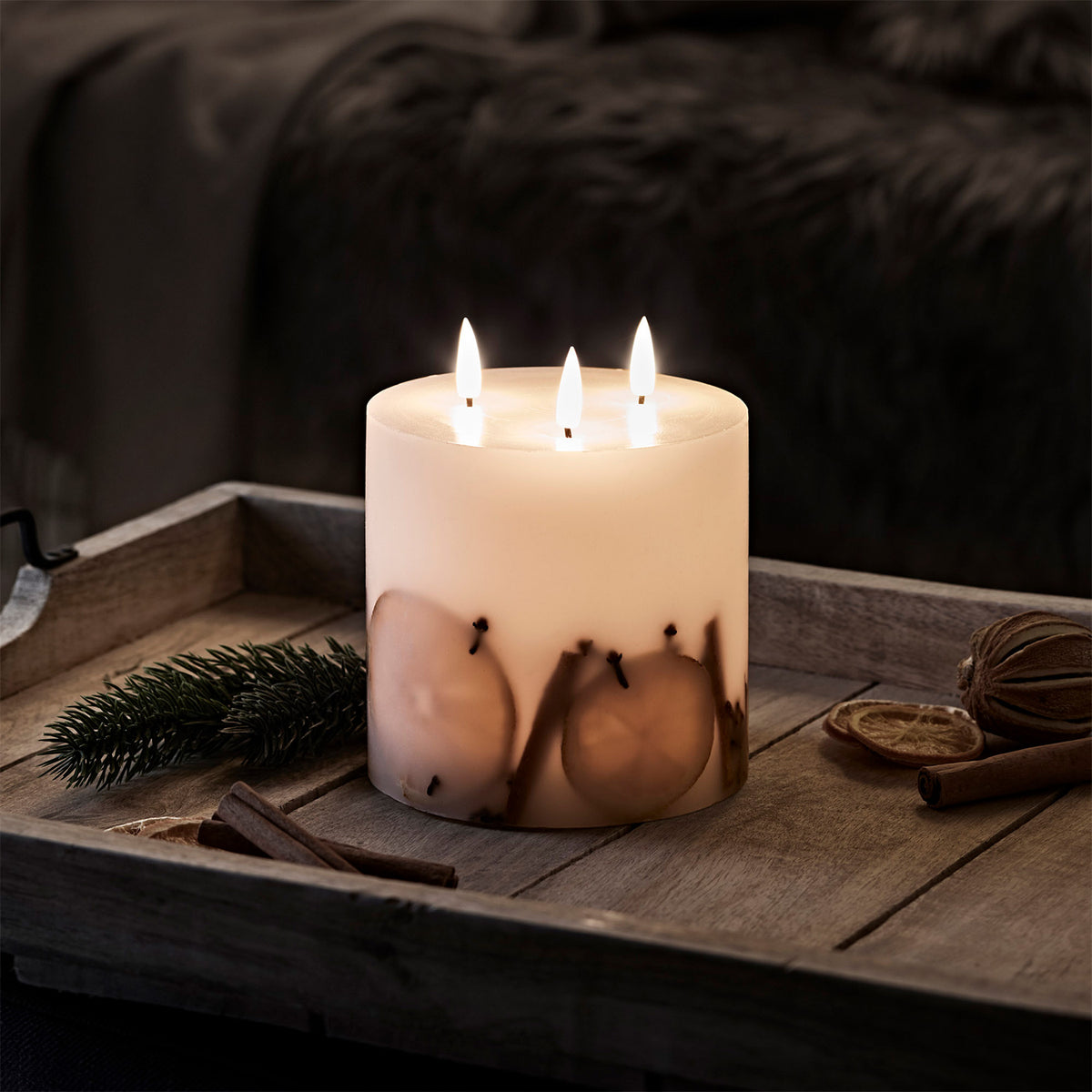 Winterliche LED-Kerze mit drei Dochten auf Holztablett mit Zimtstangen und Orangenscheiben