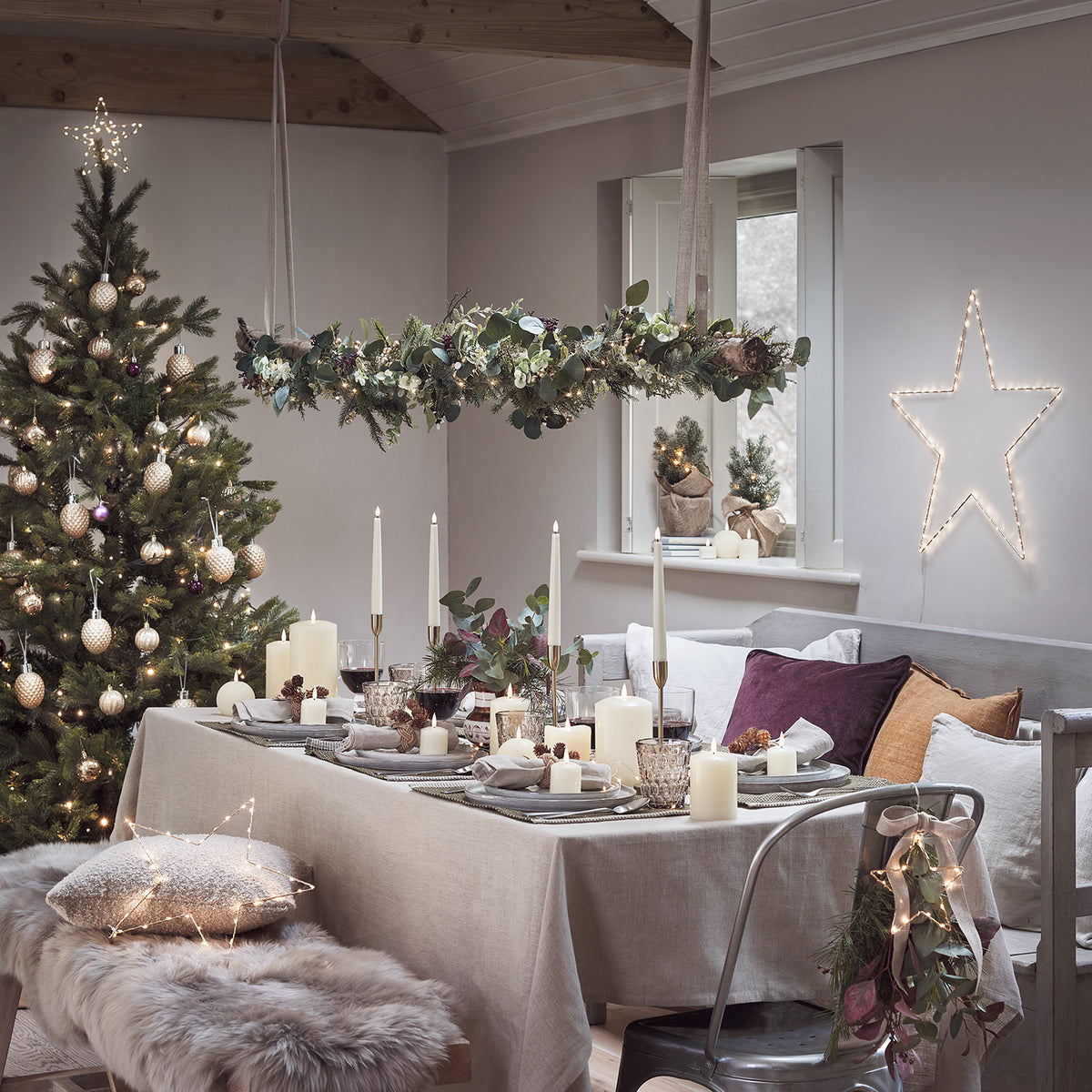 Weihnachtlich gedeckter Tisch mit vier weißen LED Stabkerzen und Weihnachtsbaum im Hintergrund