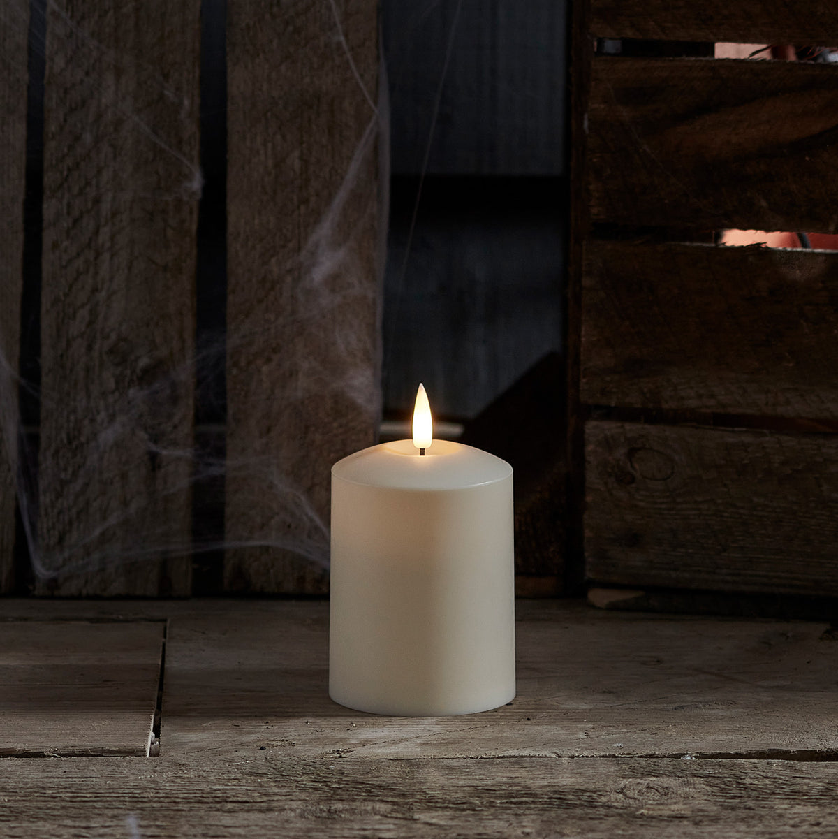 Weiße TruGlow LED Outdoor Kerze mit flackernder Flamme vor dunklem Holz