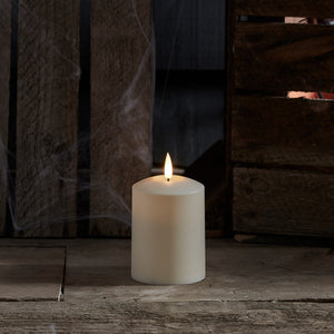 Weiße TruGlow LED Outdoor Kerze mit flackernder Flamme vor dunklem Holz