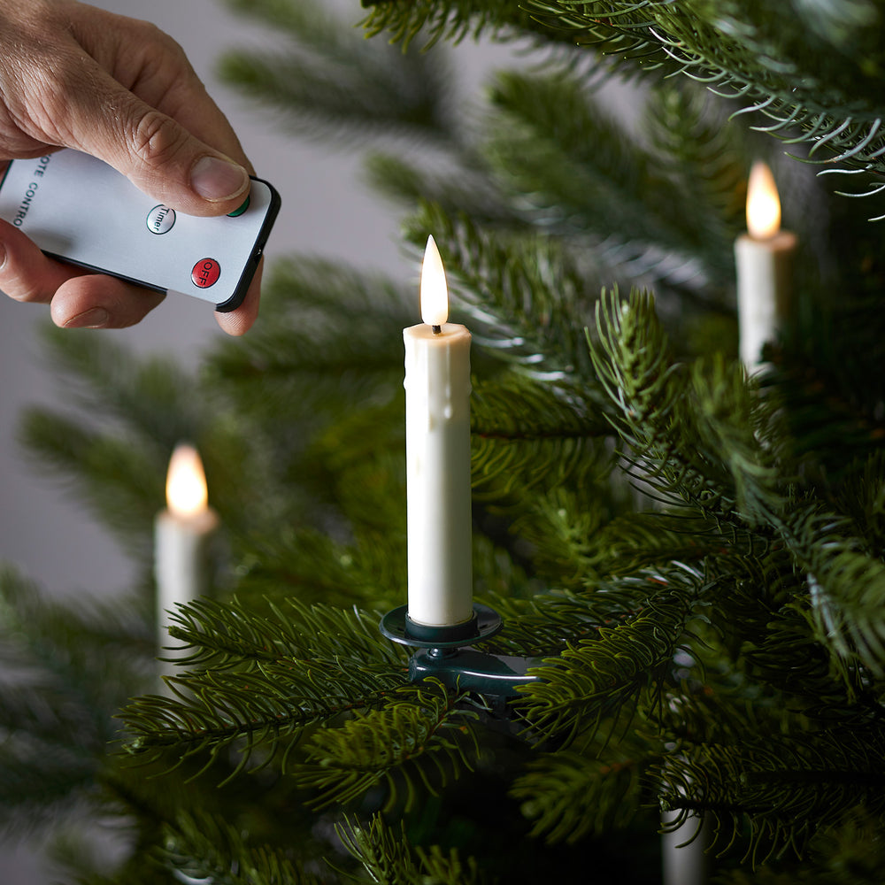 Hand mit Fernbedienung steuert LED Baumkerze auf Tannenzweig mit Flammen-LED
